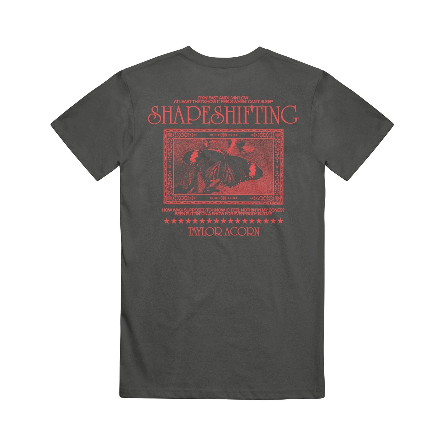 A dark gray Taylor Acorn Comfort Colors t-shirt with red graphics. The back displays SHAPESHIFTING above a butterfly illustration, framed by borders, stars, and Taylor Acorn’s name in signature printed style.