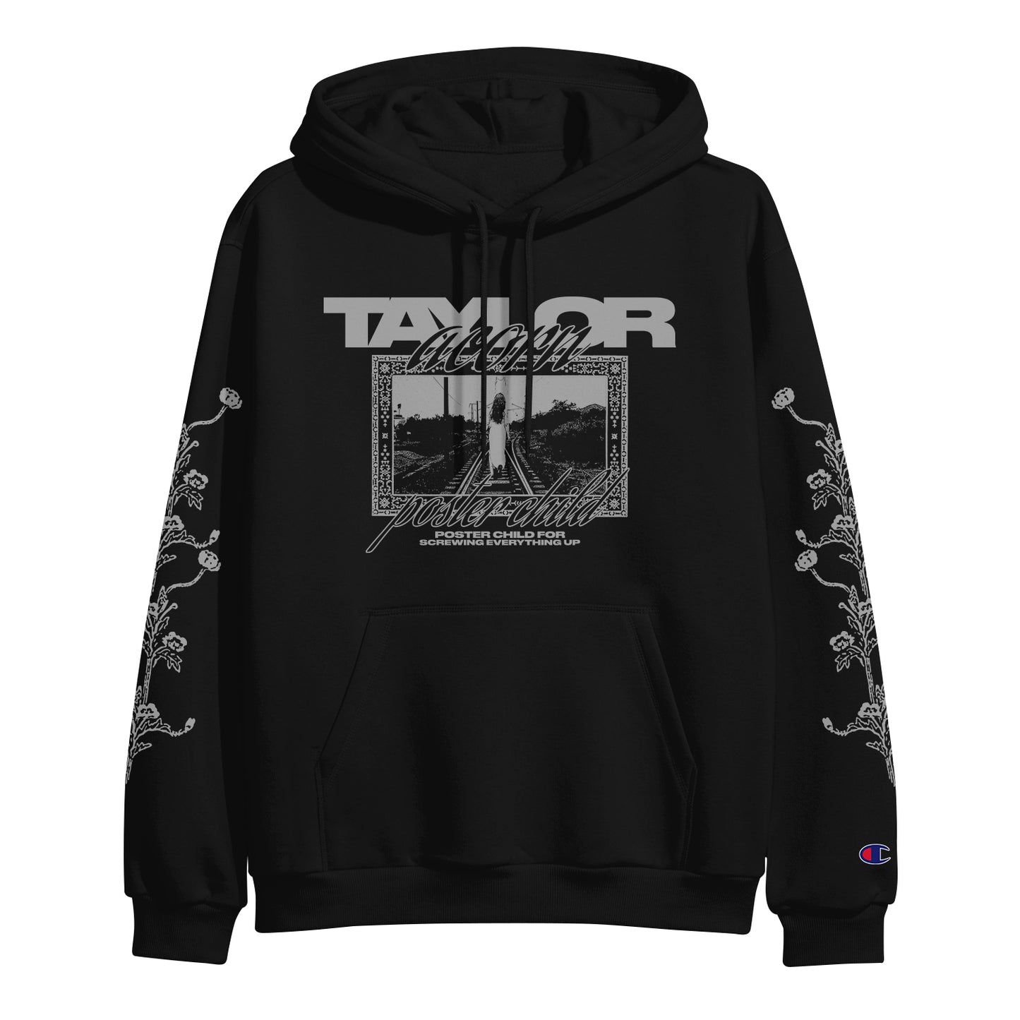 Black hooded sweatshirt by Taylor Acorn with “TAYLOR” and “album folklore” above a grayscale photo framed by decorative borders. Features floral vine patterns on both sleeves and Champion logo on the left wrist.
