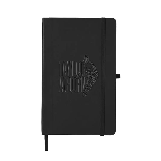 A black Taylor Acorn notebook with an embossed logo and acorn graphic, featuring an elastic closure, pen loop, and ribbon bookmark for convenience.