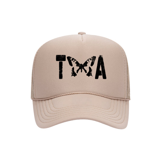 A beige Otto Cap Trucker Hat by Taylor Acorn features black T and A letters separated by a black butterfly, replacing the X. Perfect for fans of unique printed hats.