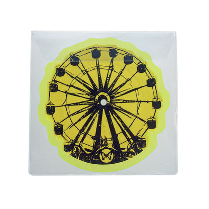A Taylor Acorn sticker with a black Ferris wheel design on a bright yellow background, packaged in a clear, square plastic sleeve.