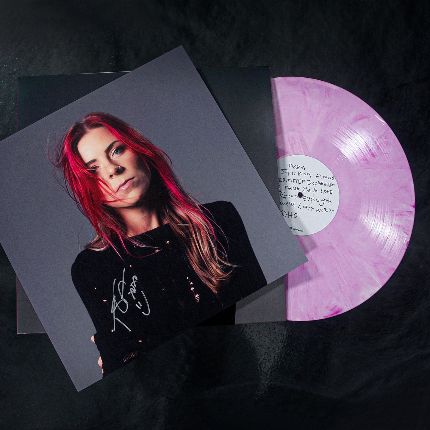 A pink and white marbled signed vinyl record by Taylor Acorn, partially out of its sleeve, featuring the Certified Depressant album cover with a woman with long red and blonde hair in a black top and a handwritten signature.