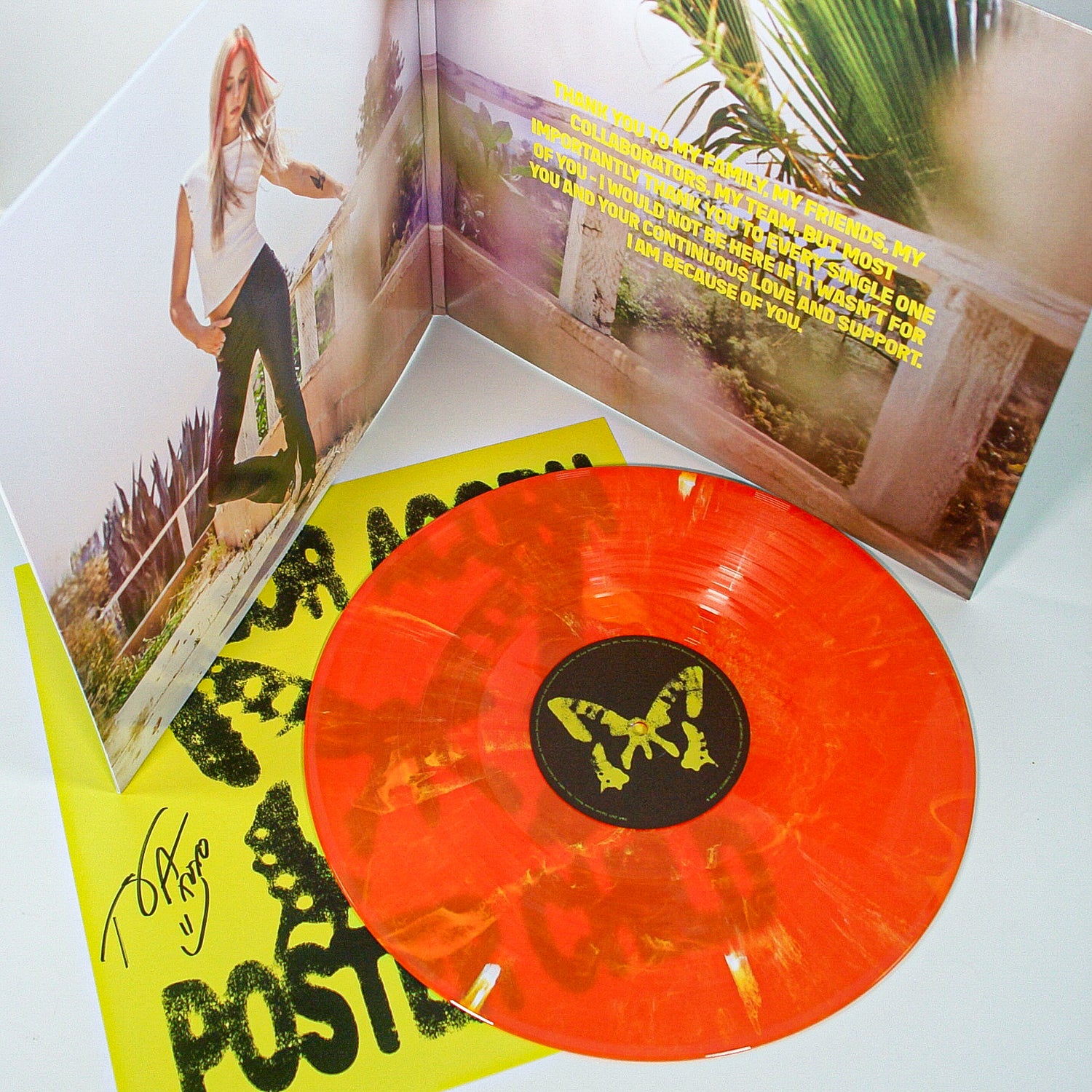 A Taylor Acorn orange marbled vinyl signed LP is shown with its gatefold jacket open, featuring a woman jumping outdoors, a thank you note, and a yellow insert with black text and a partially visible signature underneath.