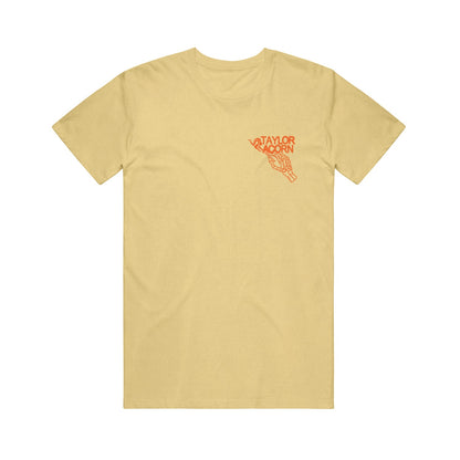 A light yellow Taylor Acorn Comfort Colors t-shirt featuring a small red graphic on the left chest of a hand holding a sign that says TAYLOR ACORN.