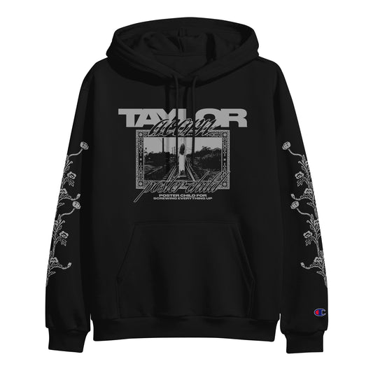 Black hooded sweatshirt by Taylor Acorn with “TAYLOR” and “album folklore” above a grayscale photo framed by decorative borders. Features floral vine patterns on both sleeves and Champion logo on the left wrist.